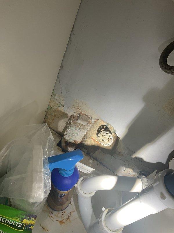 Responded to commercial water leak investigation behind interior wall. Upon inspection, discovered active moisture intrusion affecting under-sink cabinet area with visible water damage, discoloration, and potential mold growth along baseboards and corner joints. Examined PVC drain plumbing system and identified corrosion on metal pipe connections as probable leak source. Documented conditions with photographs showing extent of water damage to walls, flooring, and cabinet interior. Provided estimate for necessary repairs including wall access, pipe replacement, and water damage remediation.