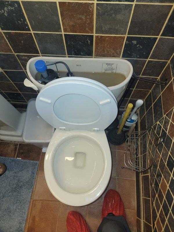 Performed toilet repair service in residential bathroom. Inspected toilet tank components and identified sediment buildup and mineral deposits affecting flush mechanism performance. Examined fill valve assembly with blue float mechanism, flush valve with overflow tube, flapper chain assembly, and water supply connections. All internal components assessed for proper operation and water flow. Tank interior showed age-related discoloration requiring attention to ensure optimal flushing performance.