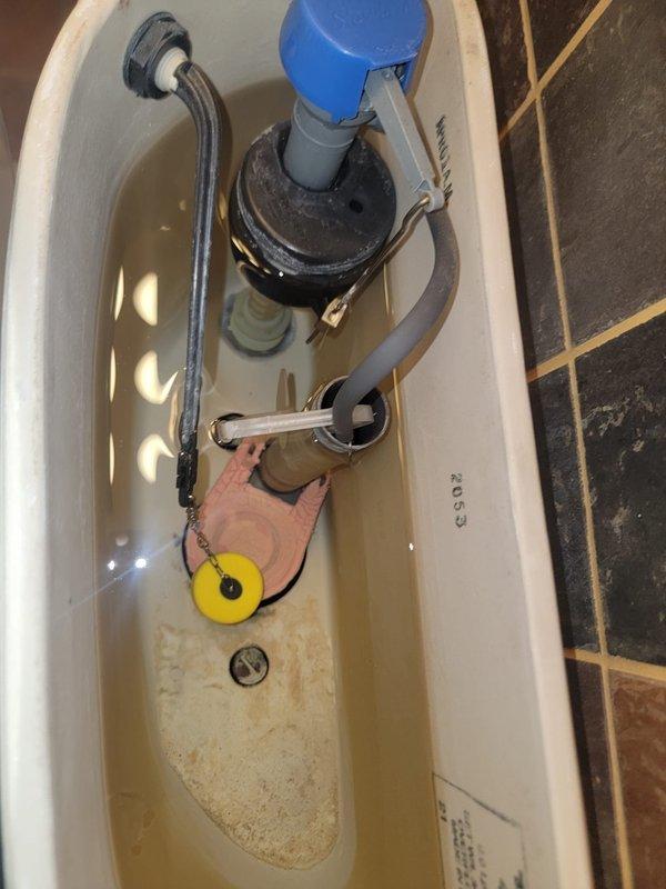 Performed toilet repair service in residential bathroom. Inspected toilet tank components and identified sediment buildup and mineral deposits affecting flush mechanism performance. Examined fill valve assembly with blue float mechanism, flush valve with overflow tube, flapper chain assembly, and water supply connections. All internal components assessed for proper operation and water flow. Tank interior showed age-related discoloration requiring attention to ensure optimal flushing performance.