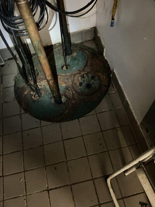 Responded to service call for sump pump alarm indicating basin filled to capacity. Upon arrival, discovered severely corroded water heater with extensive rust damage and structural deterioration requiring immediate replacement rather than sump pump issue as initially reported. Documented existing conditions showing compromised tank integrity with oxidation penetration throughout metal casing. Observed mechanical room setup with copper supply lines, electrical connections, and control panel requiring coordination for new installation. Assessed utility room layout including tile flooring, drainage access, and clearance requirements for equipment replacement to ensure code compliance and proper functionality of new system.