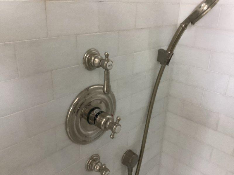 Responded to service call at 20-year-old residential property to address multiple plumbing concerns. Inspected and repaired non-functioning handle on upstairs master bathroom thermostatic shower valve with cross-handle controls. Evaluated guest bathroom shower head issue and performed necessary adjustments. Investigated knocking sounds in walls related to tankless water heater installation and identified source of water hammer. Documented existing shower fixtures including handheld shower system with slide bar and thermostatic mixing valve with dual cross-handle controls on white subway tile surround.