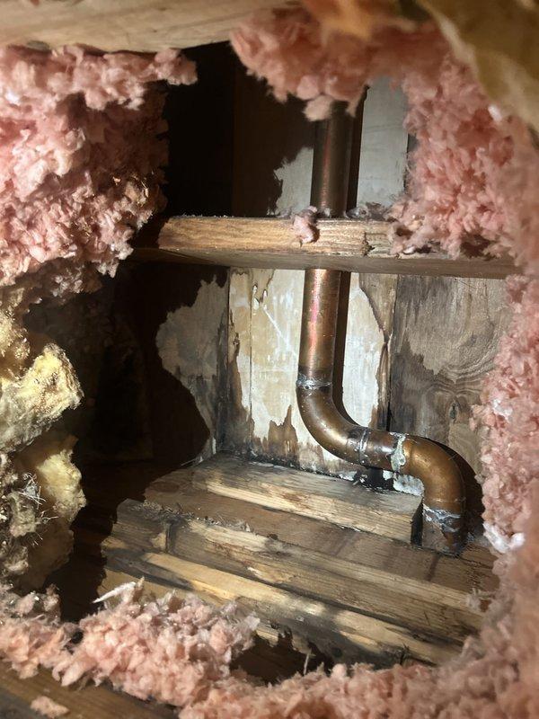 Responded to water leak investigation in multi-unit building where ceiling had been previously opened for access. Ran water through shower in unit two to reproduce leak conditions. Located source of leak at copper plumbing trap configuration within floor cavity between wooden joists. Documented findings with photographs showing copper piping, surrounding insulation, and structural framing members for repair recommendations.