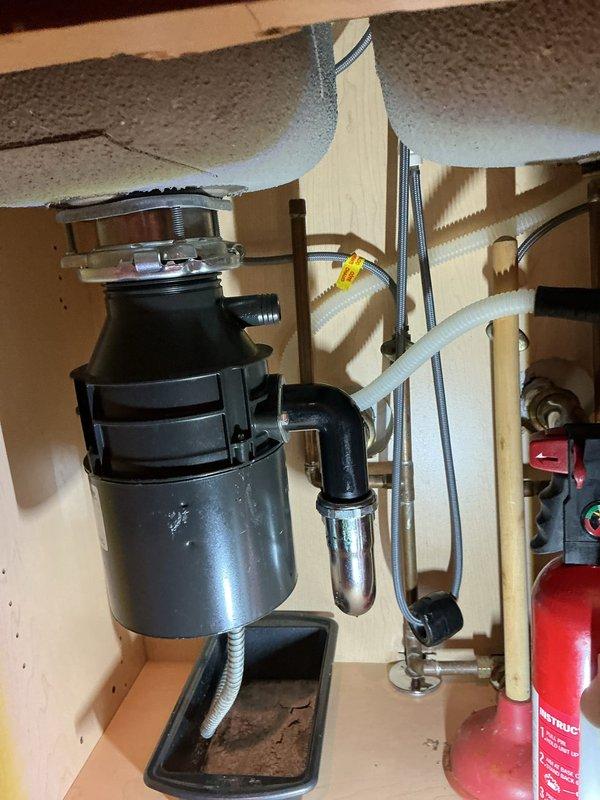 Responded to a residential plumbing service call addressing two issues: a leaking toilet caused by a pressure system malfunction within the tank, and a leaking garbage disposal unit. Upon inspection of the 25-year-old condo unit, assessed the toilet's internal pressure components and identified the source of water leakage. Examined the garbage disposal installation beneath the kitchen sink, including the mounting assembly, discharge connections, and P-trap configuration to locate the leak origin. Documented existing conditions of both fixtures, noting the age-related wear on the toilet bowl and the current plumbing setup of the disposal system with its chrome drain piping and plastic discharge components.