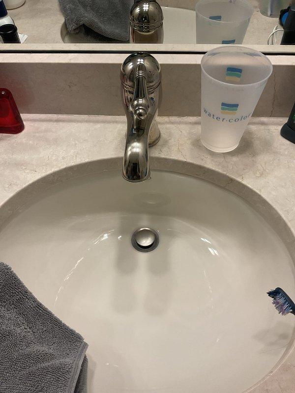 Responded to kitchen sink faucet leaking from spout following customer cleaning. Upon inspection, assessed single-handle chrome faucet in 20-year-old home for missing components or damage. Examined faucet assembly, spout connection, and internal cartridge system to identify source of leak. Documented existing conditions with photos showing bathroom vanity setup and faucet configuration for repair recommendations.