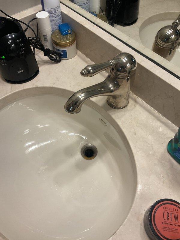 Responded to kitchen sink faucet leaking from spout following customer cleaning. Upon inspection, assessed single-handle chrome faucet in 20-year-old home for missing components or damage. Examined faucet assembly, spout connection, and internal cartridge system to identify source of leak. Documented existing conditions with photos showing bathroom vanity setup and faucet configuration for repair recommendations.