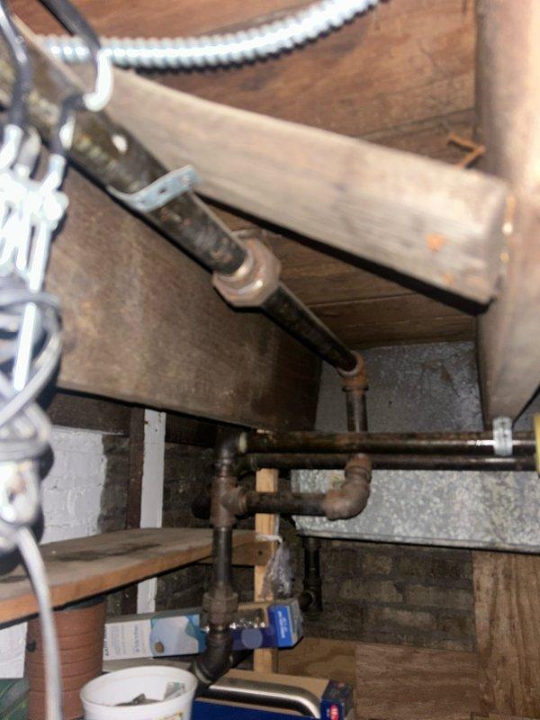 Completed plumbing estimate and inspection of existing piping system in attic crawl space. Documented aged galvanized steel pipes with visible surface corrosion, supported by wooden blocks and plastic mounting clips attached to structural framing. Photographed pipe routing, support conditions, and blue valve assembly for comprehensive assessment of system condition and replacement requirements.
