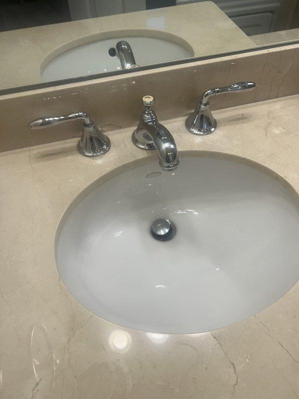 Responded to service call for bathroom faucet installation. Upon inspection, identified that a three-handle widespread chrome faucet set required installation on an undermount sink with marble countertop. Customer did not have necessary parts or components available at time of visit. Documented existing plumbing configuration including flexible braided supply lines and connection points beneath vanity. Photographed current setup showing faucet placement, drain assembly with chrome pop-up stopper, and under-sink plumbing infrastructure for reference upon return. Scheduled follow-up appointment to complete installation once customer obtains required parts.