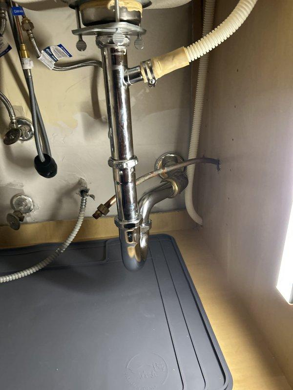 Completed warranty service call for kitchen sink water line inspection. Upon arrival, performed comprehensive assessment of under-sink plumbing system including garbage disposal unit, P-trap assembly, and water supply connections. All components found to be properly installed and functioning correctly with no visible leaks, corrosion, or damage detected. Chrome-plated drain assembly and braided metal supply lines confirmed secure with intact connections. Documented existing conditions with photographic evidence showing disposal mounting assembly, PVC drainage piping, shut-off valve, and dishwasher connection all in satisfactory working order.