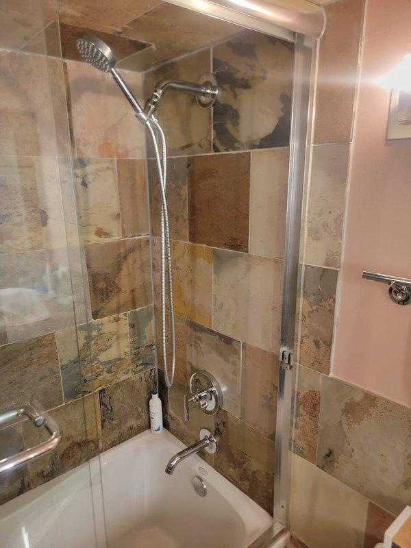Conducted on-site estimate for complete shower and bathtub plumbing fixture replacement in a 20-year-old residential property. Upon inspection, documented extensive deterioration of existing shower enclosure including significant tile damage, dark mold and mildew growth, compromised grout lines, water staining, and mineral deposits throughout the beige ceramic tile surfaces. Evaluated chrome shower assembly with handheld fixture and flexible hose, tub/shower combination with glass enclosure, and existing mixing valve and spout configuration for replacement specifications.