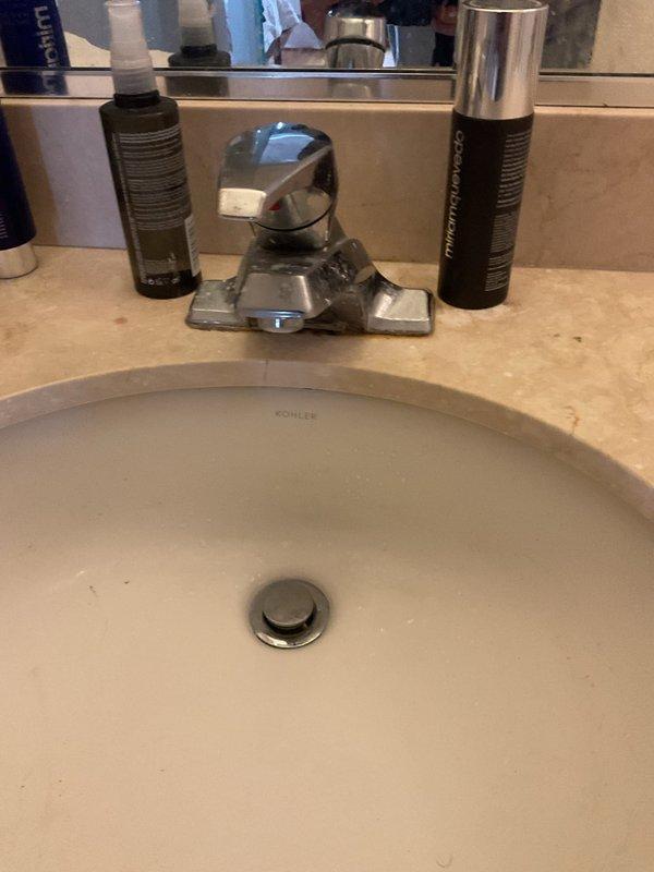 Responded to service call for bathroom sink drainage issue and dripping pop-up drain assembly. Upon inspection, found the P-trap and tailpiece assembly under the Kohler undermount sink required attention. Disassembled the chrome-plated P-trap configuration, cleared obstruction from drain line, and inspected all connections for proper sealing. Reinstalled P-trap assembly, verified wall-mounted securing brackets were properly fastened, and tested pop-up drain mechanism for proper operation and seal. Ran water through system to confirm restored drainage flow and eliminate dripping issue at drain stopper assembly.