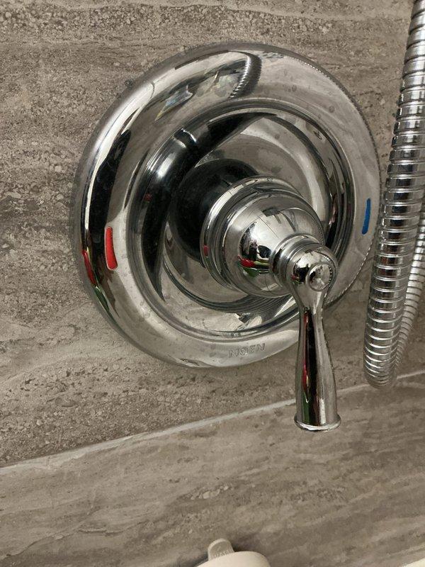 Conducted on-site assessment of existing shower fixtures in century-old home to provide replacement estimate. Evaluated current chrome-plated shower valve control with single-lever handle mounted on concrete wall, noting hot/cold indicators and handheld shower attachment. Inspected secondary shower location featuring tiled enclosure with large-format stone-pattern tiles in brick-lay arrangement, where brass/copper pipe stub extends through white escutcheon plate with chrome shower arm assembly. Documented existing fixture conditions, wall substrate types, and installation configurations through comprehensive photography to develop accurate scope of work for complete shower fixture replacement in both locations.