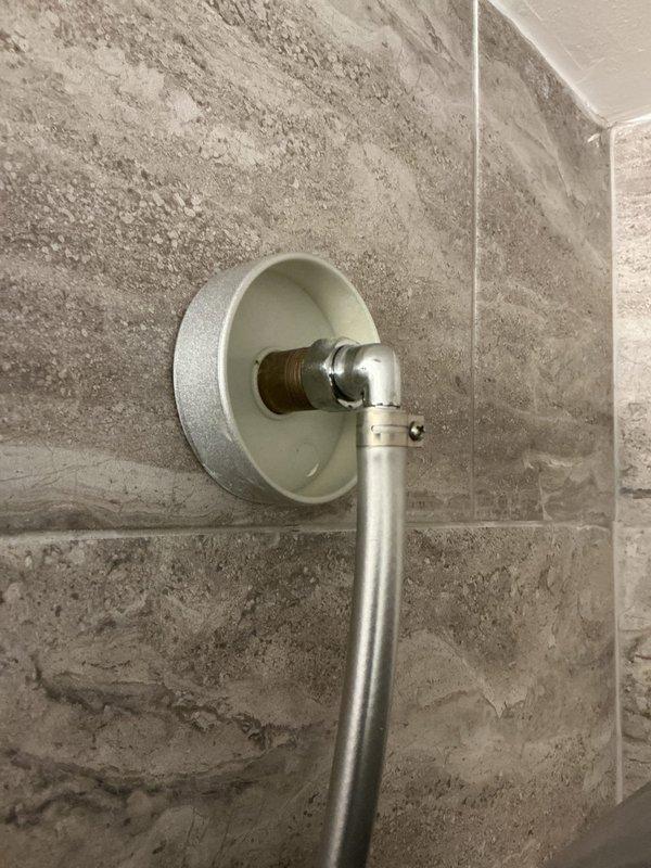 Conducted on-site assessment of existing shower fixtures in century-old home to provide replacement estimate. Evaluated current chrome-plated shower valve control with single-lever handle mounted on concrete wall, noting hot/cold indicators and handheld shower attachment. Inspected secondary shower location featuring tiled enclosure with large-format stone-pattern tiles in brick-lay arrangement, where brass/copper pipe stub extends through white escutcheon plate with chrome shower arm assembly. Documented existing fixture conditions, wall substrate types, and installation configurations through comprehensive photography to develop accurate scope of work for complete shower fixture replacement in both locations.