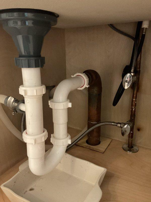 # Plumbing Service - Kitchen Sink Drain Repair

Responded to recurring failure of kitchen sink drain P-trap assembly in century-old residential property. Upon arrival, found white PVC P-trap pipe had separated from drain assembly beneath kitchen sink, marking second failure at this location within approximately one month of previous repair attempt by another service provider.

Inspection revealed the existing P-trap connections had failed due to inadequate threading engagement and potential stress from the garbage disposal unit weight distribution. Removed compromised P-trap assembly from under-sink cabinet. Assessed all threaded connections, drain tailpiece, and wall stub-out for damage or wear consistent with the property's age.

Installed new white PVC P-trap assembly with proper thread engagement at all connection points. Ensured correct alignment between garbage disposal outlet, drain tailpiece, and wall drain to prevent future stress on threaded fittings. Verified all slip-joint 