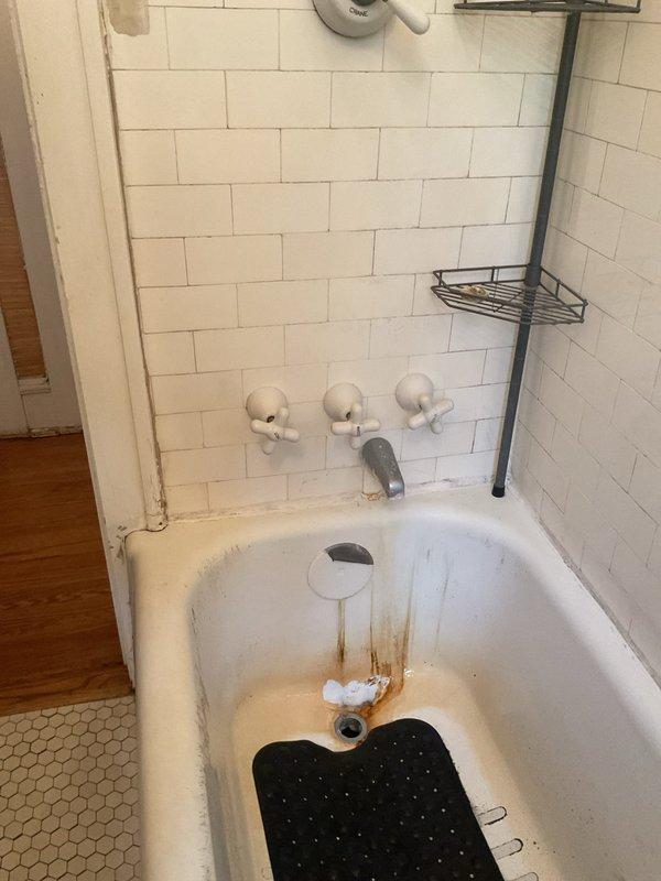 Responded to service call for leaking shower faucet that customer was unable to repair by tightening. Inspected three-handle shower valve assembly with chrome fixtures mounted on subway tile wall above bathtub. Assessed condition of valve stems, packing, and trim components. Documented existing rust staining around tub drain and mineral deposits on fixtures indicating long-term water quality issues. Photographed shower plumbing system and overall bathroom condition for estimate preparation.