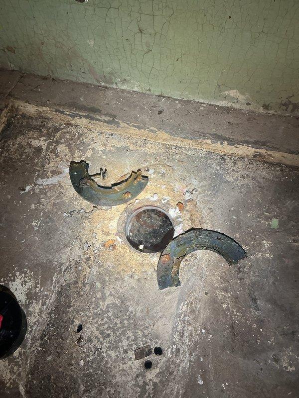 Removed existing toilet from basement bathroom and identified multiple code and structural deficiencies requiring permit work. Found cracked toilet flange with only two anchor bolts causing fixture instability and water seepage. Inspection revealed deteriorated clay drain pipe requiring replacement with PVC, necessitating concrete floor demolition and subsequent repair. Assessment determined new wax ring seal and proper flange installation will be required upon completion of rough-in work. Documented conditions with photographs showing corroded flange components, damaged flooring, and deteriorated wall surfaces for permit application and scope development.