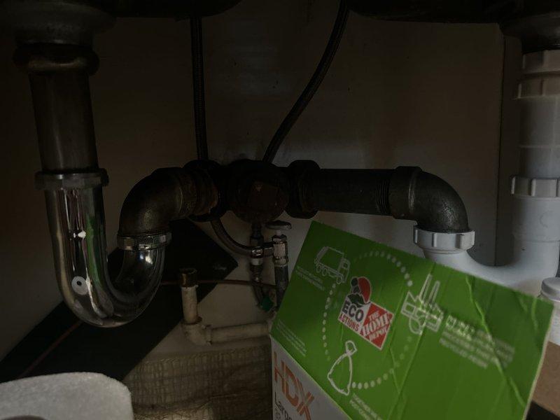 Responded to kitchen sink drainage issue where water was backing up in both compartments. Upon inspection, found compromised drain assembly under kitchen sink with aged P-trap and corroded elbow connections causing obstruction. Cleared blockage from drain line and assessed additional plumbing concerns throughout property including corroded water main with active leak, failed toilet seals, deteriorating hose bib shutoff valve, rotted chrome drain assembly at upstairs sink, and slow-filling toilet with worn internal mechanisms. Documented conditions with photographs showing extent of corrosion on main water line and degraded kitchen drain components. Provided recommendations for comprehensive repairs including pipe freeze method for water main replacement due to shared water shutoff serving multiple units in complex.