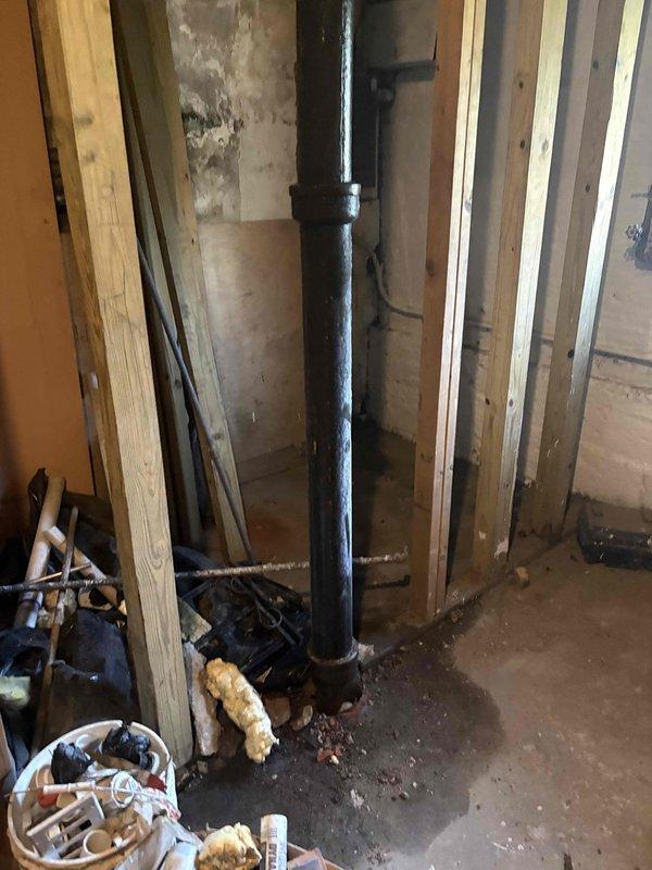 Conducted on-site assessment of residential plumbing stack system requiring repair in basement area. Inspection revealed deteriorated drainage stack with visible aging and structural concerns in unfinished basement space. Documented existing conditions including black metal drainage pipe running vertically through the space, exposed wooden floor joists, and multiple utility lines including insulated water supply pipes. Evaluated structural support elements surrounding the stack including load-bearing columns and cross-bracing. Photographed current plumbing configuration, pipe conditions, and accessibility constraints within the confined workspace. Assessed debris and construction materials present in the work area that would require clearing for stack replacement. Prepared comprehensive estimate for stack repair work including necessary access considerations and coordination with existing building systems.