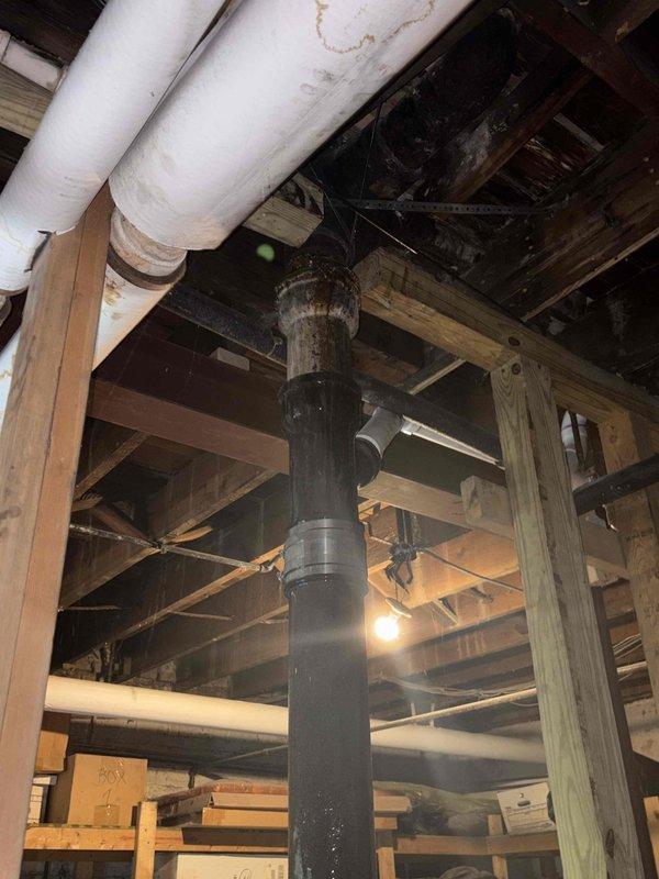 Conducted on-site assessment of residential plumbing stack system requiring repair in basement area. Inspection revealed deteriorated drainage stack with visible aging and structural concerns in unfinished basement space. Documented existing conditions including black metal drainage pipe running vertically through the space, exposed wooden floor joists, and multiple utility lines including insulated water supply pipes. Evaluated structural support elements surrounding the stack including load-bearing columns and cross-bracing. Photographed current plumbing configuration, pipe conditions, and accessibility constraints within the confined workspace. Assessed debris and construction materials present in the work area that would require clearing for stack replacement. Prepared comprehensive estimate for stack repair work including necessary access considerations and coordination with existing building systems.