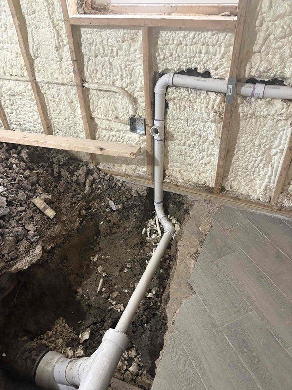 Completed estimate for residential ADU with improperly installed underground plumbing system. Previous plumber had excavated trenches correctly, but underground plumbing connections were not executed to code. Inspected interior construction area with exposed framing and spray foam insulation where white PVC drain lines run vertically and horizontally through excavated floor sections containing soil, rocks, and debris. Evaluated T-joint configurations and pipe routing emerging from and descending into trenched areas adjacent to existing concrete flooring. Documented current plumbing installation conditions to provide accurate estimate for correcting underground drainage system deficiencies and bringing work into compliance with applicable plumbing codes.