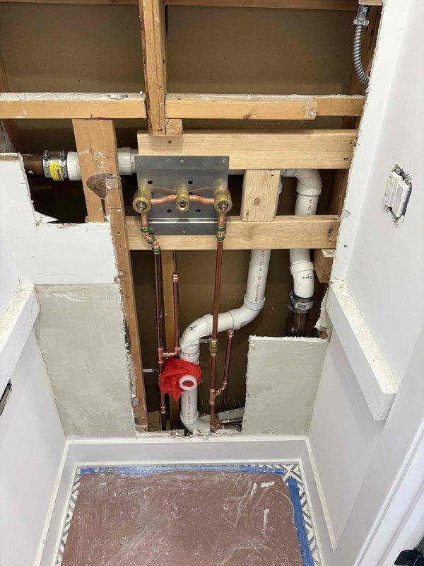 Completed rough-in plumbing installation for new faucet assembly in residential setting. Installed copper supply lines with brass fittings, PVC drain lines with proper venting, and mounting plate secured to wall framing. Added shut-off valve assembly and water hammer arrestor for system protection.