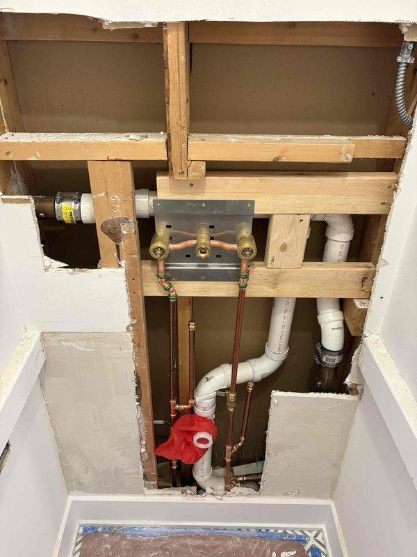 Completed rough-in plumbing installation for new faucet assembly in residential setting. Installed copper supply lines with brass fittings, PVC drain lines with proper venting, and mounting plate secured to wall framing. Added shut-off valve assembly and water hammer arrestor for system protection.