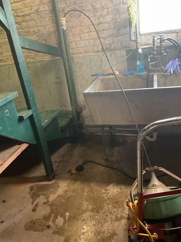 Responded to a clogged basement slop sink complaint. Upon inspection, found the stainless steel double-basin utility sink experiencing drainage issues with visible staining and residue buildup throughout both compartments. Successfully cleared the obstruction from the drain line, restoring proper water flow and drainage function to the fixture.