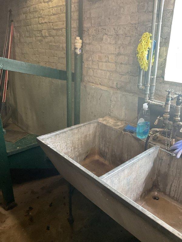 Responded to a clogged basement slop sink complaint. Upon inspection, found the stainless steel double-basin utility sink experiencing drainage issues with visible staining and residue buildup throughout both compartments. Successfully cleared the obstruction from the drain line, restoring proper water flow and drainage function to the fixture.
