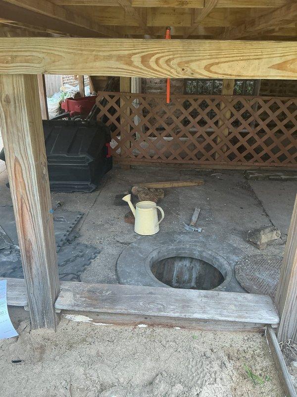 Responded to customer request for main drain cleanout installation and hydrojetting estimates. Inspected existing drainage access point located in outdoor utility structure with plywood construction and foam mat flooring. Evaluated circular floor access opening leading to deteriorated concrete sump pit approximately two feet in diameter. Documented extensive concrete degradation including vertical cracking, efflorescence, water staining, and mineral deposits throughout cylindrical structure. Observed standing water and sediment accumulation at bottom of pit with visible mounting hardware on interior walls. Assessed feasibility of installing new cleanout port at this exterior location versus alternative basement installation beneath concrete floor. Photographed existing conditions showing weathered concrete infrastructure and access limitations within wooden shed structure to provide accurate estimate for cleanout installation and hydrojetting services.