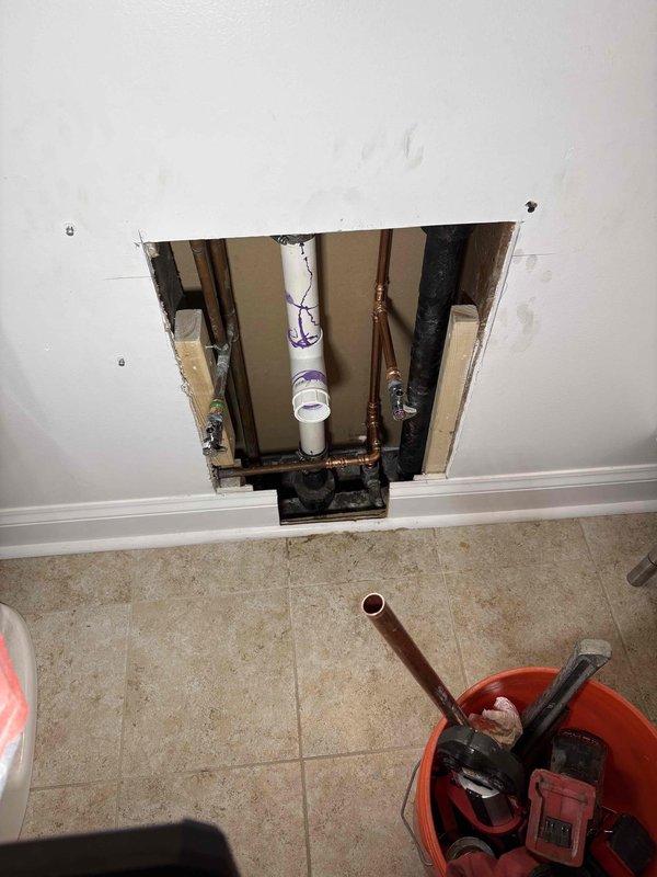 Responded to service call for bathroom sink water line repair. Upon inspection, accessed plumbing infrastructure through wall cavity near floor level to locate the source of the leak. Identified compromised connection point between copper supply line and black pipe section serving the bathroom sink. Repaired the defective threaded fitting and connection to restore proper water flow to the fixture. Verified all connections were secure and tested system for leaks before closing access point.
