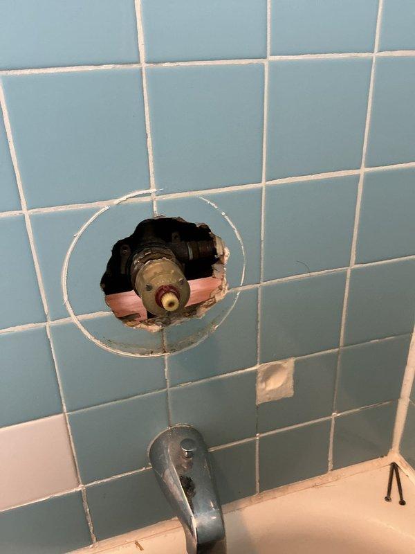 Responded to water leak and low hot water pressure issues in 125-year-old condo building. Accessed plumbing system through bathroom wall by removing section of light blue tile surround to expose valve assembly and supply lines. Repaired leaking water main valve serving washing machine connection. Diagnosed and resolved severely restricted hot water flow issue that developed following recent building water heater repair, restoring proper hot water pressure throughout unit. Reinstalled access point and completed testing to verify both leak elimination and adequate hot water flow restoration.