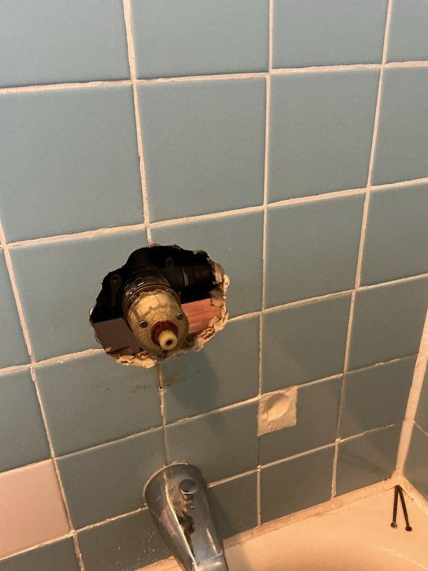 Responded to water leak and low hot water pressure issues in 125-year-old condo building. Accessed plumbing system through bathroom wall by removing section of light blue tile surround to expose valve assembly and supply lines. Repaired leaking water main valve serving washing machine connection. Diagnosed and resolved severely restricted hot water flow issue that developed following recent building water heater repair, restoring proper hot water pressure throughout unit. Reinstalled access point and completed testing to verify both leak elimination and adequate hot water flow restoration.