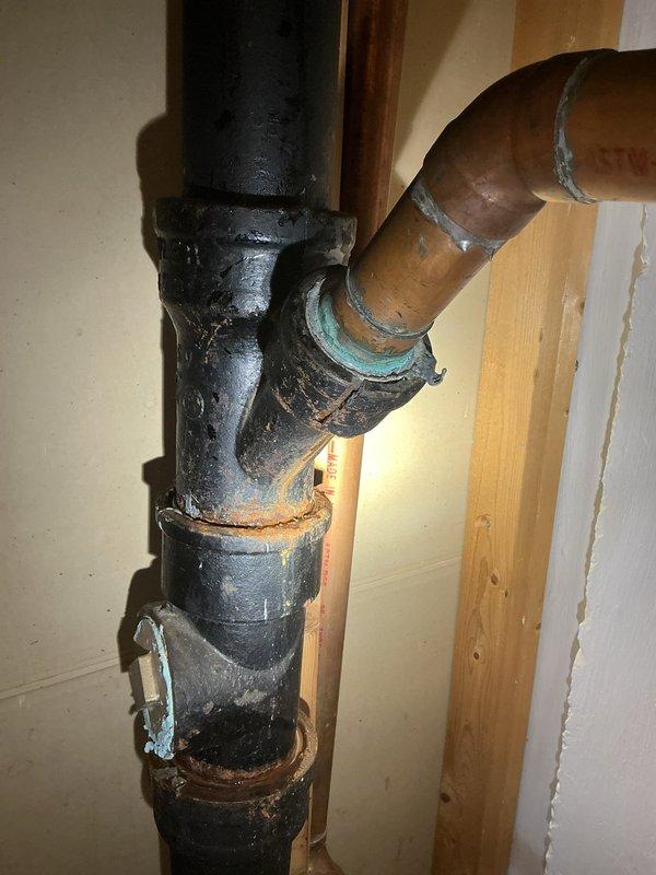Completed plumbing estimate for sump pump area with deteriorated drainage and supply lines. Documented existing conditions including severely corroded cast iron vertical drain pipe with failing connections, oxidized copper supply lines with verdigris buildup at joints, and mixed PVC/copper configuration requiring assessment. The inspection revealed aging plumbing infrastructure with compromised pipe integrity, corroded fittings, and potential leak points at connection interfaces that will need replacement to ensure proper sump pump operation and prevent water damage.