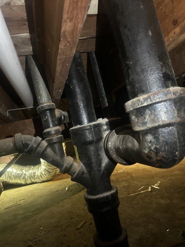 Responded to a commercial drain and sewer estimate for a basement bathroom leak affecting the ceiling below. Upon inspection of the exposed ceiling cavity, identified severely corroded cast iron drain piping with visible rust and deterioration, indicating long-term moisture exposure and potential failure points. The plumbing system showed multiple pipe connections and junctions in the unfinished ceiling space, with aging black steel pipes, PVC components, and compromised metal sections requiring evaluation for replacement to prevent continued water damage and restore proper drainage function.
