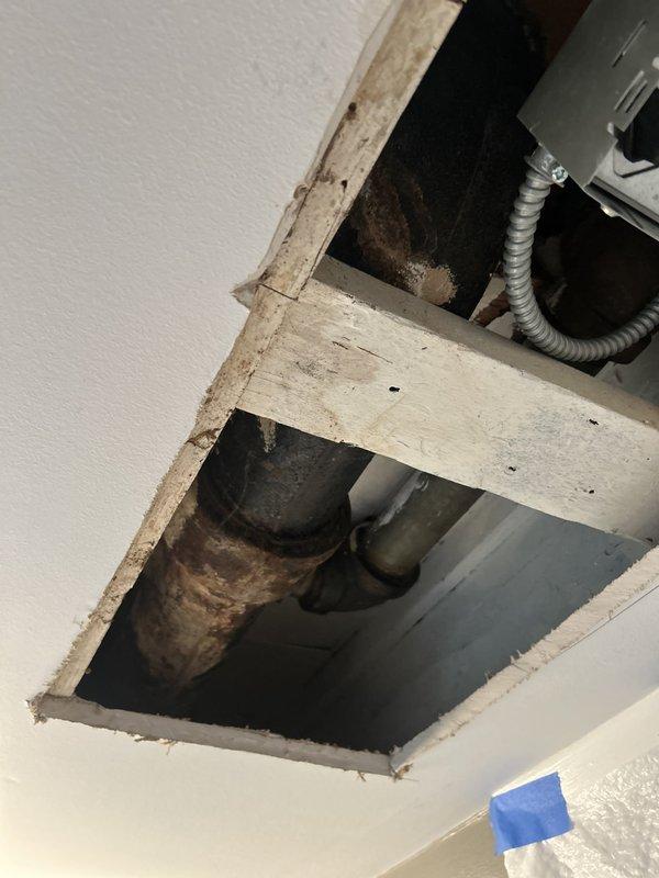 Responded to a commercial drain and sewer estimate for a basement bathroom leak affecting the ceiling below. Upon inspection of the exposed ceiling cavity, identified severely corroded cast iron drain piping with visible rust and deterioration, indicating long-term moisture exposure and potential failure points. The plumbing system showed multiple pipe connections and junctions in the unfinished ceiling space, with aging black steel pipes, PVC components, and compromised metal sections requiring evaluation for replacement to prevent continued water damage and restore proper drainage function.