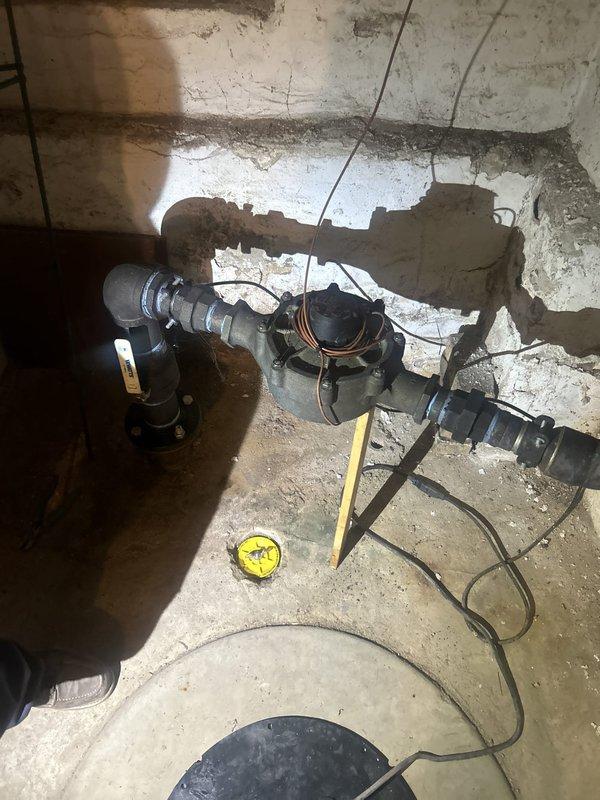 Responded to water leak call at century-old residential property. Upon arrival, conducted thorough inspection of plumbing infrastructure in basement mechanical room. Located active leak at main water meter assembly, where aged corrugated piping connections showed signs of deterioration and compromised seals. 

Assessed secondary plumbing fixtures in bathroom area, identifying additional concerns with vintage brass valve assemblies featuring blue-handled shutoffs. Observed significant mineral deposits, corrosion, and water staining around drain opening and mounting surfaces, indicating chronic moisture exposure consistent with slow leak conditions over extended period.

Performed emergency repairs to water meter connections, replacing deteriorated gaskets and tightening compression fittings to restore watertight seal. Tested system under full pressure to verify leak elimination. Documented existing conditions of aged brass fixtures and recommended monitoring for future service needs due