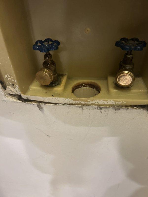 Responded to water leak call at century-old residential property. Upon arrival, conducted thorough inspection of plumbing infrastructure in basement mechanical room. Located active leak at main water meter assembly, where aged corrugated piping connections showed signs of deterioration and compromised seals. 

Assessed secondary plumbing fixtures in bathroom area, identifying additional concerns with vintage brass valve assemblies featuring blue-handled shutoffs. Observed significant mineral deposits, corrosion, and water staining around drain opening and mounting surfaces, indicating chronic moisture exposure consistent with slow leak conditions over extended period.

Performed emergency repairs to water meter connections, replacing deteriorated gaskets and tightening compression fittings to restore watertight seal. Tested system under full pressure to verify leak elimination. Documented existing conditions of aged brass fixtures and recommended monitoring for future service needs due