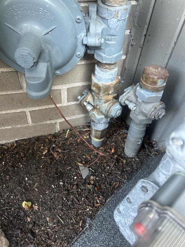 Responded to gas leak service call and conducted thorough inspection of exterior gas meter and piping system. Upon examination, identified aging threaded connections and deteriorating pipe coatings on the utility connection assembly at the building's foundation, along with a penetration point through the masonry wall containing a brass fitting. Performed pressure testing on the gas line system to verify system integrity and locate source of reported leak.