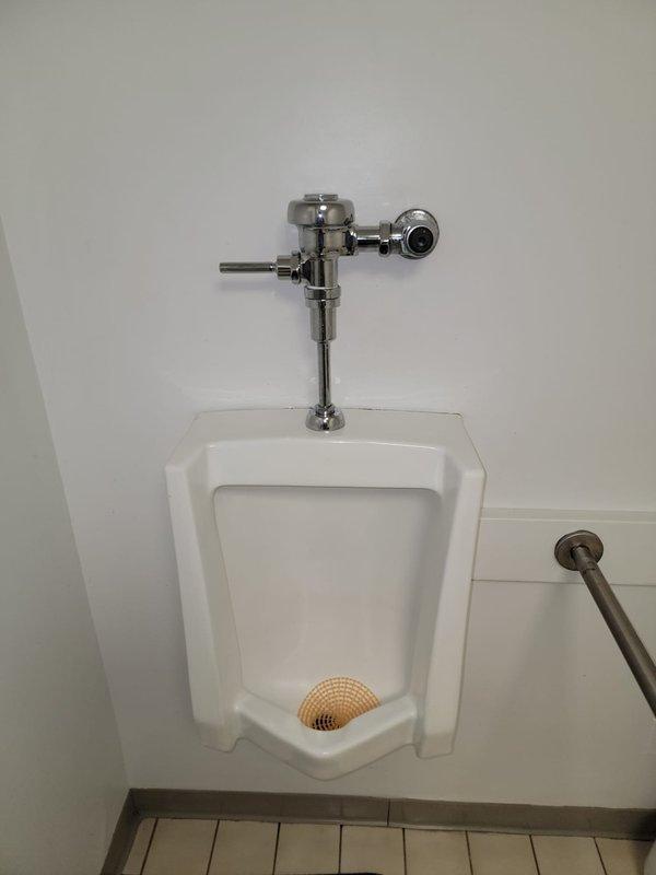 Responded to a commercial men's restroom for a continuously running urinal. Upon arrival, confirmed the isolation valve had been closed by facility staff to stop water flow. Inspected the wall-mounted urinal and chrome flush valve assembly. Diagnosed faulty flushometer diaphragm causing constant water discharge. Replaced diaphragm kit, reassembled flush valve mechanism, restored water supply, and tested operation. Verified proper flush cycle and complete water shutoff. Unit now functioning normally with no leaks detected.