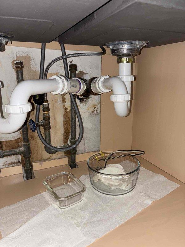 Responded to service call for newly installed kitchen sink experiencing slow drainage and leaking. Upon inspection, identified improper drain assembly installation beneath sink causing water backup and leakage into cabinet. Disassembled and reconfigured PVC P-trap connections to ensure proper drainage slope and secure sealing at all threaded joints. Verified chrome strainer basket connection at sink drain outlet and tightened to eliminate leak points. Tested water flow through system and confirmed drainage operating at normal speed with no leaks present. Cleaned cabinet interior of water staining and addressed moisture damage from previous leak exposure. Also scheduled for dishwasher installation at future appointment.