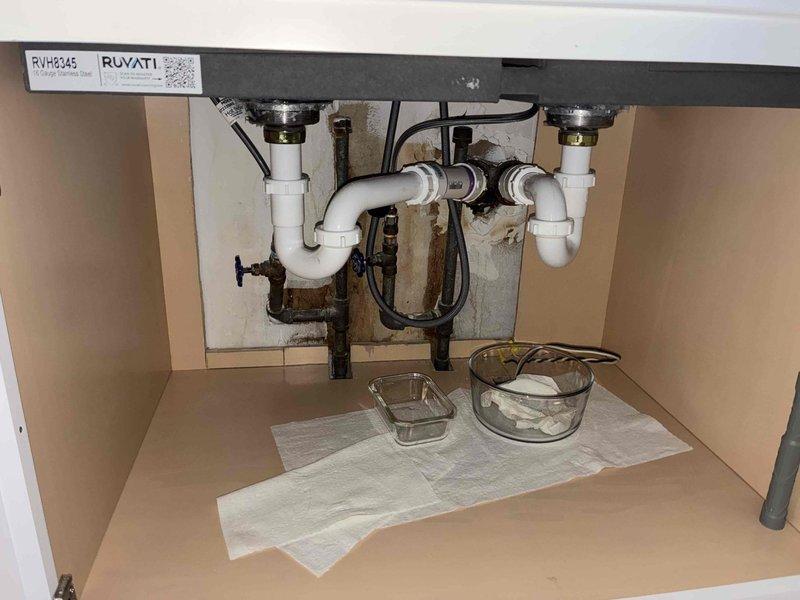 Responded to service call for newly installed kitchen sink experiencing slow drainage and leaking. Upon inspection, identified improper drain assembly installation beneath sink causing water backup and leakage into cabinet. Disassembled and reconfigured PVC P-trap connections to ensure proper drainage slope and secure sealing at all threaded joints. Verified chrome strainer basket connection at sink drain outlet and tightened to eliminate leak points. Tested water flow through system and confirmed drainage operating at normal speed with no leaks present. Cleaned cabinet interior of water staining and addressed moisture damage from previous leak exposure. Also scheduled for dishwasher installation at future appointment.