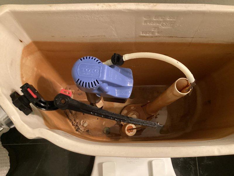 Responded to service call for toilet tank not filling properly in a 29-year-old residential property. Upon inspection, found the existing fill valve mechanism had failed due to age and significant mineral buildup throughout the tank interior. Removed the old blue Fluidmaster-style fill valve assembly and replaced it with a new fill valve unit featuring updated components and improved water flow regulation. Adjusted the refill tube connection to the overflow tube to ensure proper bowl refill after flushing. Tested the flush valve chain mechanism and flapper seal for proper operation. Verified all internal components were functioning correctly, with the tank now filling to appropriate water level and shutting off properly. The new fill valve assembly includes a red adjustment cap for easy future height modifications if needed. System restored to full operational status with proper fill cycle and water shut-off functionality.