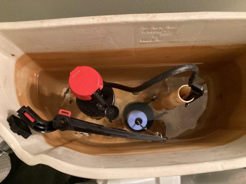 Responded to service call for toilet tank not filling properly in a 29-year-old residential property. Upon inspection, found the existing fill valve mechanism had failed due to age and significant mineral buildup throughout the tank interior. Removed the old blue Fluidmaster-style fill valve assembly and replaced it with a new fill valve unit featuring updated components and improved water flow regulation. Adjusted the refill tube connection to the overflow tube to ensure proper bowl refill after flushing. Tested the flush valve chain mechanism and flapper seal for proper operation. Verified all internal components were functioning correctly, with the tank now filling to appropriate water level and shutting off properly. The new fill valve assembly includes a red adjustment cap for easy future height modifications if needed. System restored to full operational status with proper fill cycle and water shut-off functionality.