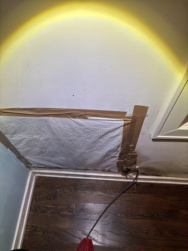 Responded to water leak concern in middle bedroom where customer reported mold growth along bottom wall. Upon inspection, confirmed significant mold contamination on white cabinet base and adjacent wall surfaces near floor level, indicating prolonged moisture intrusion. Documented extensive dark gray-black mold growth with characteristic fuzzy texture spanning cabinet lower panel and baseboard area. Installed protective coverings and began moisture remediation protocol. Set up air filtration equipment and dehumidification system to control airborne spores and reduce ambient moisture levels. Investigation revealed water source requiring further assessment to determine if leak originates from exterior window penetration, interior plumbing, or foundation moisture wicking through wall assembly.