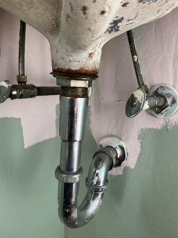 # Plumbing Repair - Indoor Sink Drain Assembly

Responded to service call for reported outdoor spigot leak when hot water was activated. Upon inspection, determined the actual issue was located at an interior bathroom sink installation. Assessed the existing drain assembly, which exhibited significant age-related deterioration including rust staining on the sink basin underside and tarnished chrome fittings throughout the P-trap configuration.

Performed comprehensive evaluation of the drain tailpiece, P-trap assembly, and associated supply line connections. Identified compromised seals and corroded connection points as the source of water infiltration. The existing pop-up drain mechanism showed wear consistent with extended service life. Wall-mounted supply valves and shutoff connections were inspected for proper function and potential contribution to moisture issues.

Completed necessary repairs to restore proper drainage function and eliminate water leakage. Work included addressing