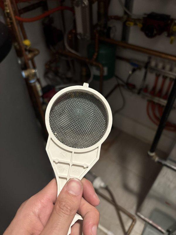 Responded to service call for recently installed boiler displaying error code. Upon arrival, inspected boiler system and identified clogged inlet filter as source of malfunction. Removed and cleaned white plastic strainer component with fine mesh screen from water supply line. Filter showed debris accumulation restricting water flow, which triggered low water pressure error on boiler control board. Flushed filter housing, reinstalled clean filter with gasket properly seated, and restored water supply to unit. Cleared error code from boiler system, verified proper operation, and confirmed adequate water flow through all connections. System tested and returned to normal operating parameters.