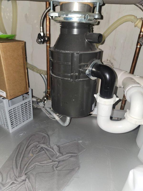 Responded to service call for leaking garbage disposal and kitchen faucet repair. Removed and replaced defective garbage disposal unit with new black disposal, securing mounting assembly to sink drain with proper flange connection. Connected discharge line to existing P-trap configuration using white PVC drainage pipes. Verified electrical connection and tested unit for proper operation and drainage. Inspected kitchen faucet and replaced worn cartridge to restore proper function and eliminate dripping. Tested all plumbing connections under sink for leaks, confirmed proper water flow, and verified garbage disposal grinding operation. All systems functioning correctly upon completion.