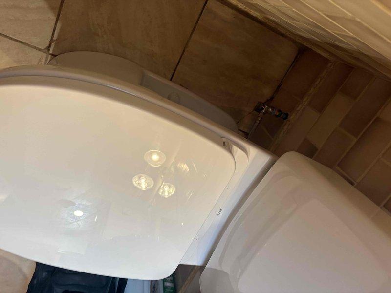 Completed installation of a new two-piece white porcelain toilet in residential bathroom with brown and beige subway tile walls and tan ceramic floor tiles. Toilet was properly positioned, secured, and tested to ensure proper function and no leaks upon completion.