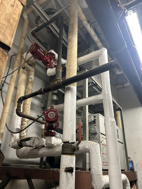 Performed inspection and assessment of commercial HVAC and mechanical systems. Evaluated Copper-Fin II unit in mechanical room, documenting equipment condition, safety labels, and operational specifications. Inspected extensive piping network including insulated white pipes, circulating pumps, valves, and associated connections throughout the mechanical space. Photographed equipment configuration and system components for service records and future reference.