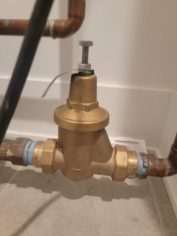Responded to commercial plumbing service warranty call for operational sump pump system. Upon arrival, conducted thorough inspection of sump pump installation and associated components. Verified proper electrical wiring routing along interior wall junction with secure cable management. Inspected pressure reducing valve assembly with brass body and compression fittings on copper piping, confirming appropriate pressure regulation settings and valve functionality. Documented system configuration and component conditions through photographic documentation. All equipment found operating within normal parameters with no immediate service requirements identified.
