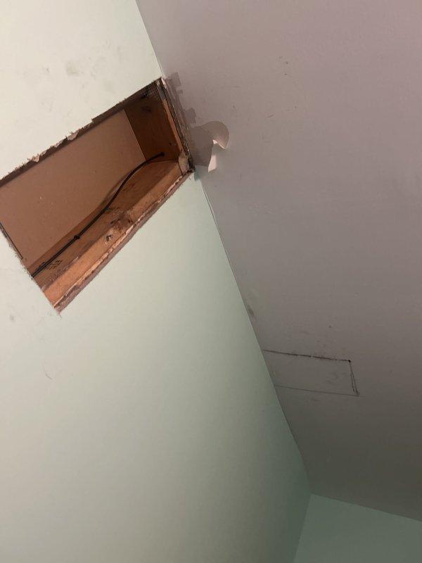 Responded to apartment water leak investigation request. Upon arrival, conducted thorough visual inspection of affected areas and identified active water intrusion evidenced by ceiling staining and discoloration with brownish-gray water marks concentrated around rectangular access panel area. Created exploratory opening in wall near ceiling junction to access concealed plumbing and structural components for source identification. Inspection revealed moisture damage to wooden framing members behind finished drywall surfaces. Documented conditions with photographic evidence showing extent of water damage to ceiling surfaces and exposed structural elements. Located leak source within concealed plumbing system accessible through investigation opening. Provided findings and recommendations for necessary repairs to address water intrusion and restore affected areas.